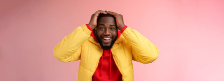 Waist-up surprised happy lucky young african-american bearded male in yellow jacket holding hands...