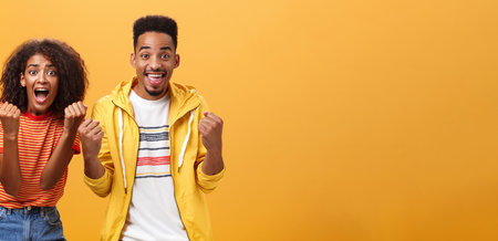 Two friends cheering and supporting mate on competition yelling joyfully clenching fists in supportive geture smiling broadly waiting with amazement and excitement for win and victoryの写真素材