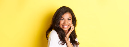 Image of beautiful african-american woman, smiling flirty and touching face, advertising beauty...