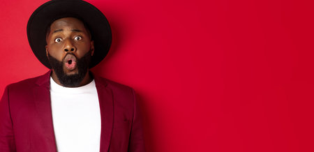 Close-up of surprised Black man staring at camera with wonder, standing against red background