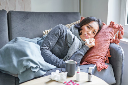 Sick woman lying on sofa at home, catching cold. Young girl freezing from heating problem in her...