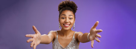 Close-up charming touched tender wealthy african-american woman in silver fashionable dress extend arms towards camera give warm welcome hug smiling delighted wanna cuddle hold in handsの写真素材
