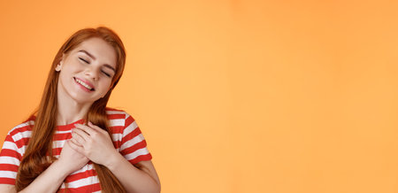 Close-up lovely caring tender redhead girlfriend feel love, close eyes smiling toothy silly grin, press palms heart, feel touched, daydreaming, have feelings, confess sympathy tasty foodの写真素材