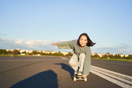 Skater girl riding on skateboard, standing on her longboard and laughing, riding cruiser on an empty...