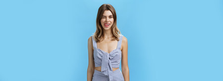 Portrait of cute woman with natural hairstyle in matching clothes winking flirty showing tongue on upper lip and smiling tricky being in playful romantic mood feeling happy and joyful over grey wallの写真素材