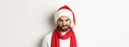 New Year party and winter holidays concept. Close-up of grumpy guy in santa hat frowning and...
