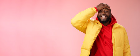 Charming cute black bearded 25s guy forget something stupid silly smiling friendly punch forehead grinning feel awkward say sorry standing pink background joyfully relaxedの写真素材