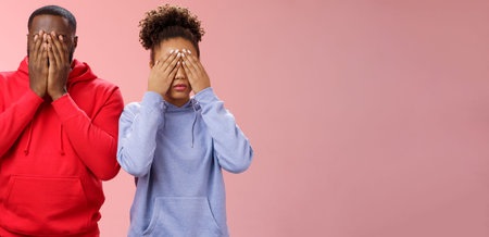 Two african-american man woman standing pink background hide faces close eyes palms tired looking...