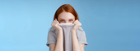 Silly flirty amused attractive playful redhead girlfriend hiding face pulling t-shirt head squinting...