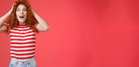 Astonished surprised emotive happy redhead girl receive incredible offer gift grab curly hair open mouth smiling amazed stunned amazing cool opportunity triumphing win red backgroundの写真素材