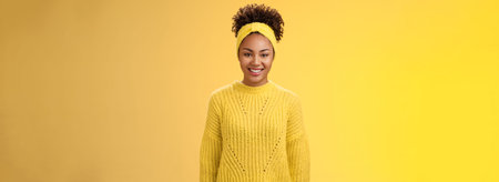 Charismatic friendly smiling black girl headband curly afro hairstyle grinning joyfully excited participate univertisy event helping out standing outgoing energized yellow backgroundの写真素材