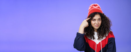 Close-up shot of confused and annoyed woman being shocked with weird and stupid behaviour rolling index finger over temple and looking questioned at camera as wonder of dumb friend ideasの写真素材