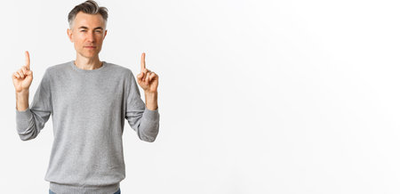 Image of thoughtful and unsure adult man, squinting hesitant while pointing fingers up, making...