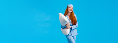 Full-length vertical studio cheerful lovely caucasian woman with ginger red long hair in nightwear, pyjama and sleep mask, hugging pillow ready sleep going bed at nigh and laughing, smilingの写真素材