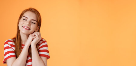 Silly dreamy redhead girl, look hopeful, press palms together lovely near cheek close eyes, daydreaming imaging dad buys new smartphone after graduation, fantasizing, remember good memoriesの写真素材