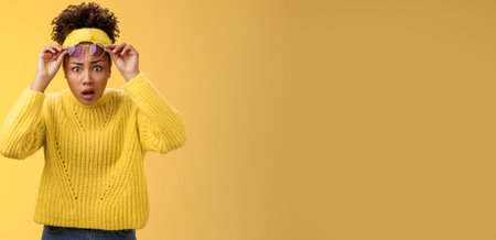 What heck. Shocked stunned confused african-american stylish modern girl in sweater headband take-off sunglasses widen eyes surprise speechless gasping look questioned freak-out, yellow backgroundの写真素材