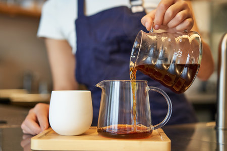 Close up of glass jar and a cup standing on cafe counter, barista pouring filter coffee and preparing orderの写真素材