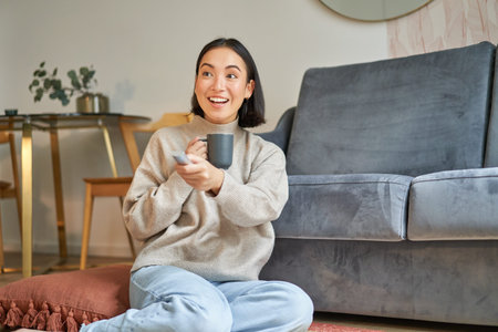 Portrait of smiling young woman resting at home near tv, watching television sitting on floor and...