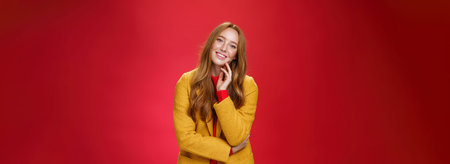 Good-looking carefree and happy relaxed redhead girlfriend in yellow stylish coat touching face and...