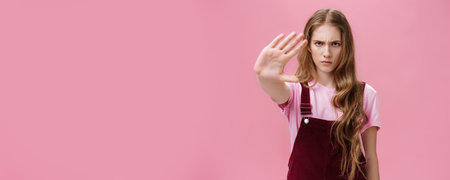 Woman protest against testing products on animals. Serious-looking confident young girl with long wavy hair frowning looking sctrict at camera pulling palm towards camera in prohibition and no gestureの写真素材