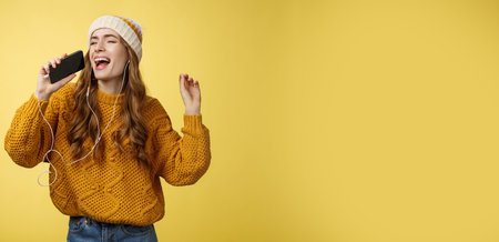 Carefree charming girl likes karaoke having fun listen favorite songs wearing wired earphones hold smartphone microphone singing out loud dancing enjoying spend time aloneの写真素材