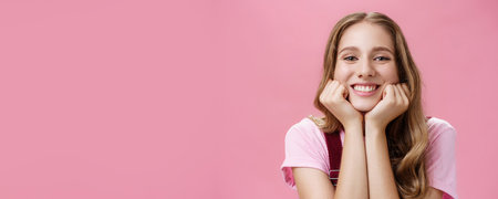 Cute feminine and tender nice girl withtattoo and wavy hair leaning head on hands as if listening amusing story gazing with broad smile and admiration gaze being dreamy over pink backgroundの写真素材