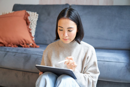Creative young woman sitting with tablet and pen, drawing on digital applicationの写真素材