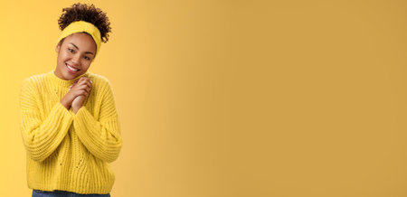 Touched tender african-american woman press palms together sighing happily smiling enjoying lovely scene grinning look passionate delighted grateful have united supportive family, yellow backgroundの写真素材