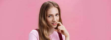 Cute feminine girl learning how make glances and seduce boyfriend with flirty gaze biting finger sensually posing against pink background, flirting making senducing look wearing make-up on dateの写真素材