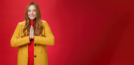 Girl welcomes us with buddhist namaste gesture pressing palms together over chest smiling friendly and delighted with carefree emotions holding hands in pray, posing happily over red backgroundの写真素材
