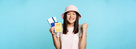 Happy asian girl triumphing, showing vaccination certificate, health passport and flight tickets,...