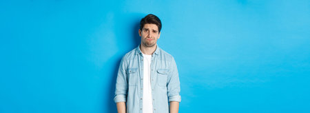 Man looking with doubt at camera, frowning and sulking, feeling uneasy about something, standing...
