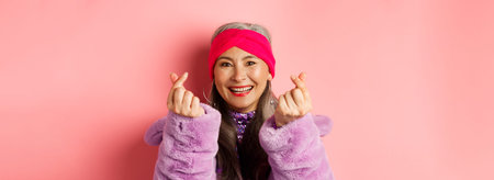 Fashion. Beautiful and fashionable asian senior woman smiling, showing korean heart gesture and...