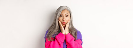 Close up of fashionable asian senior woman with grey hair looking surprised, saying wow and staring...