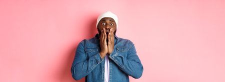 Alarmed and worried Black man staring at bad accident, gasping and standing in panic over pink backgroundの写真素材