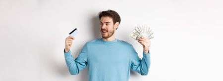 Handsome bearded man choosing between money and plastic credit card, payment with cash or...