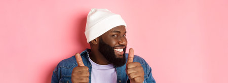 Close-up of happy Black bearded guy in beanie showing support, agree or approve something, giggle...