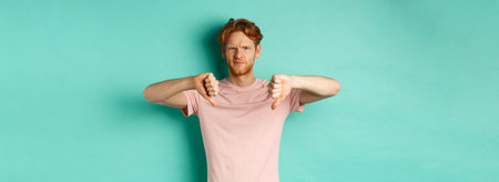 Disappointed guy with red hair showing thumbs-down, frowning and looking skeptical, epxress dislike...