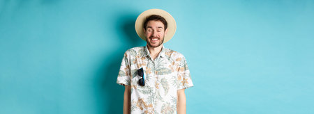 Happy tourist enjoying summer holiday, wearing straw hat and hawaiian shirt, standing joyful on blue...