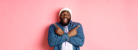 Excited young african-american man pointing sideways, showing two choices and making decision, smiling happy, standing over pink backgroundの写真素材