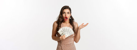 Shopping concept. Image of beautiful woman in glamour dress looking shocked, holding dollars and...