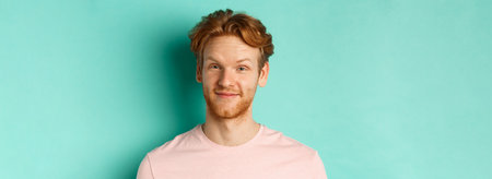 Close up of redhead bearded man looking pleased, nod in approval and smiling, standing in pink t-shirt against turquoise backgroundの写真素材