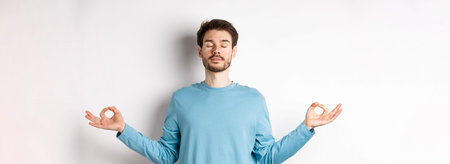 Young man trying to relax in meditation, standing calm with stretch out hands in zen mudra gesture,...