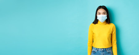 Covid-19, social distancing and pandemic concept. Teenage asian woman in medical mask, looking at...