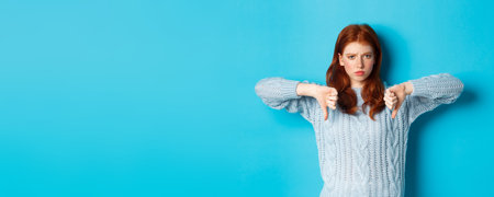 Disappointed redhead girl in sweater showing thumbs-down, judging bad product, disagree and dislike...