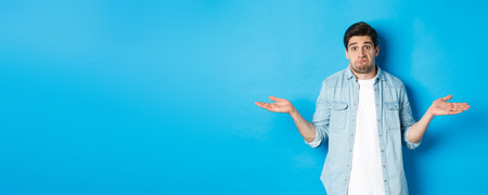 Confused young man in casual clothes shrugging, dont know anything, looking clueless, standing...