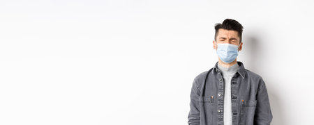 Health, covid and pandemic concept. Sad crying man in medical mask feeling upset about quarantine, standing on white backgroundの写真素材