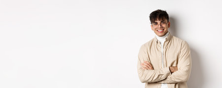 Handsome young man in glasses cross arms on chest, smiling at camera carefree, standing on white backgroundの写真素材