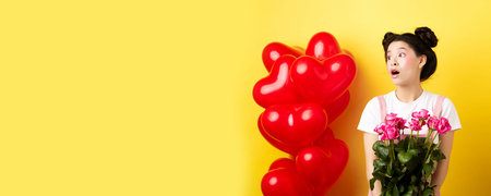 Happy Valentines day. Surprised asian girl looking left with silly face, holding cute pink flowers,...