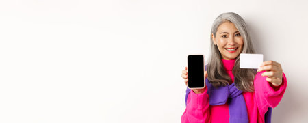 Online shopping. Close-up of stylish korean senior woman showing empty mobile screen and plastic...